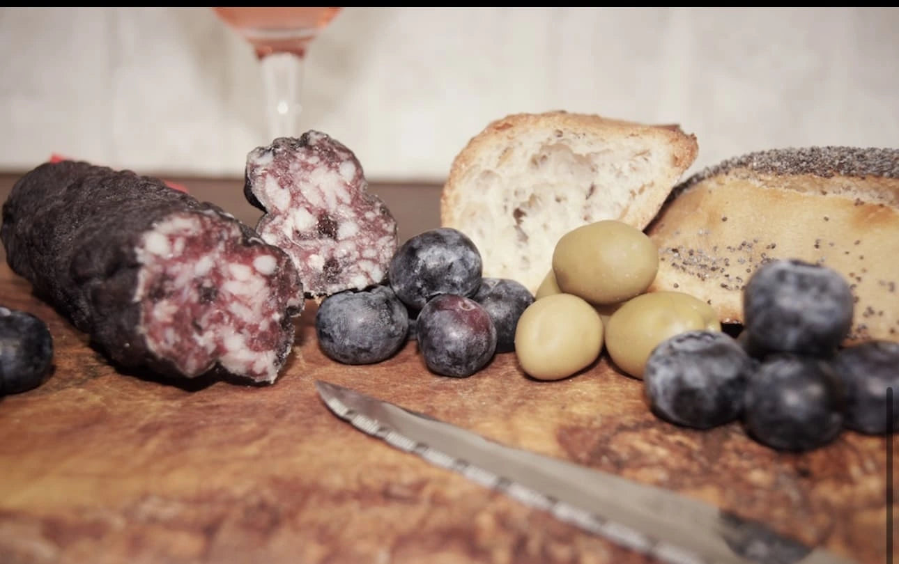 Saucisson à la myrtille coupé, myrtilles fraîches, olives et pain sur planche en bois, alliance sucré-salé pour l’apéro.