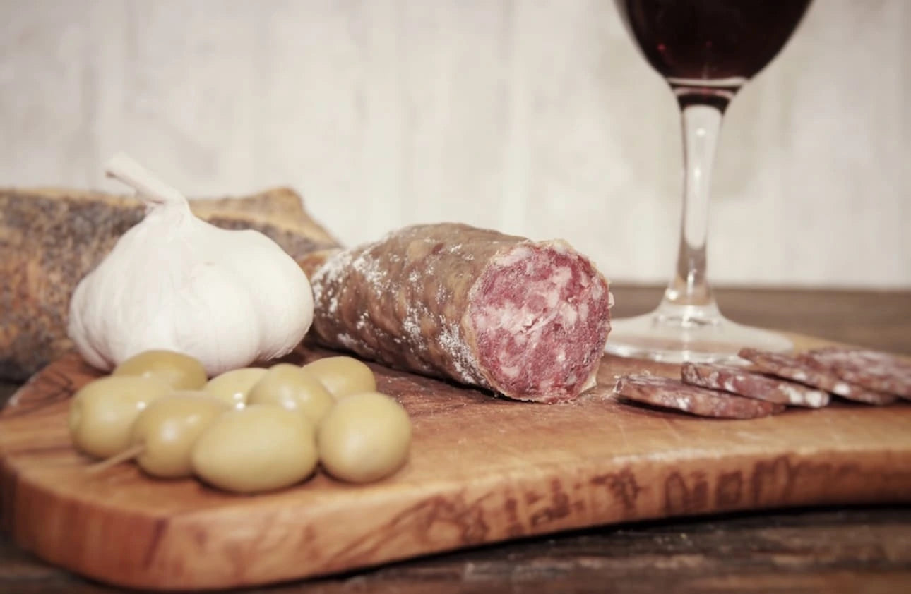 Saucisson à l’ail entamé sur planche, gousse d’ail, olives et pain, charcuterie rustique idéale pour l’apéritif.