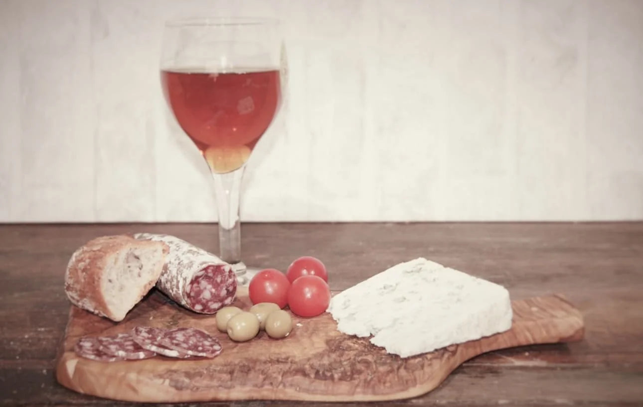 Saucisson au Roquefort tranché avec pain, tomates cerises, olives et verre de boisson ambrée — association charcuterie et fromage bleu.
