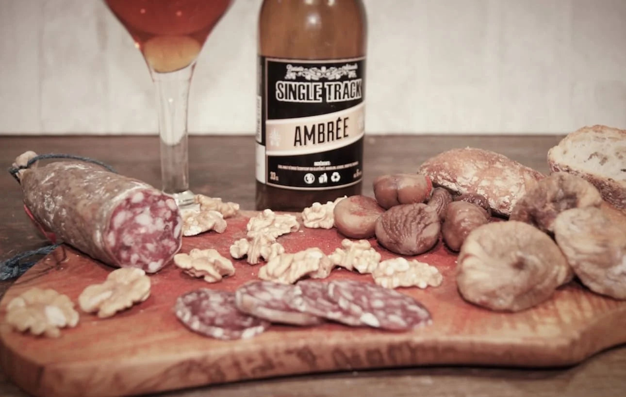 Saucisson campagnard tranché avec noix, figues sèches, pain rustique et bière ambrée — plateau de charcuterie du terroir.
