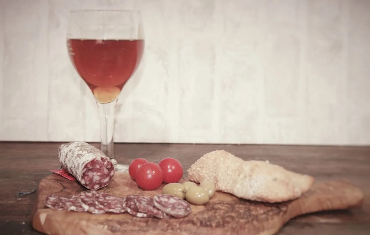 Saucisson de canard séché, tranches fines sur planche en bois avec olives, tomates et pain — apéritif gourmand et authentique.